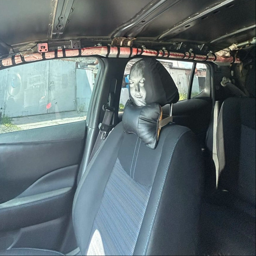 A black car interior ceiling and roof lining with a padded headrest or pillow mounted near the rear window, shown inside a vehicle.